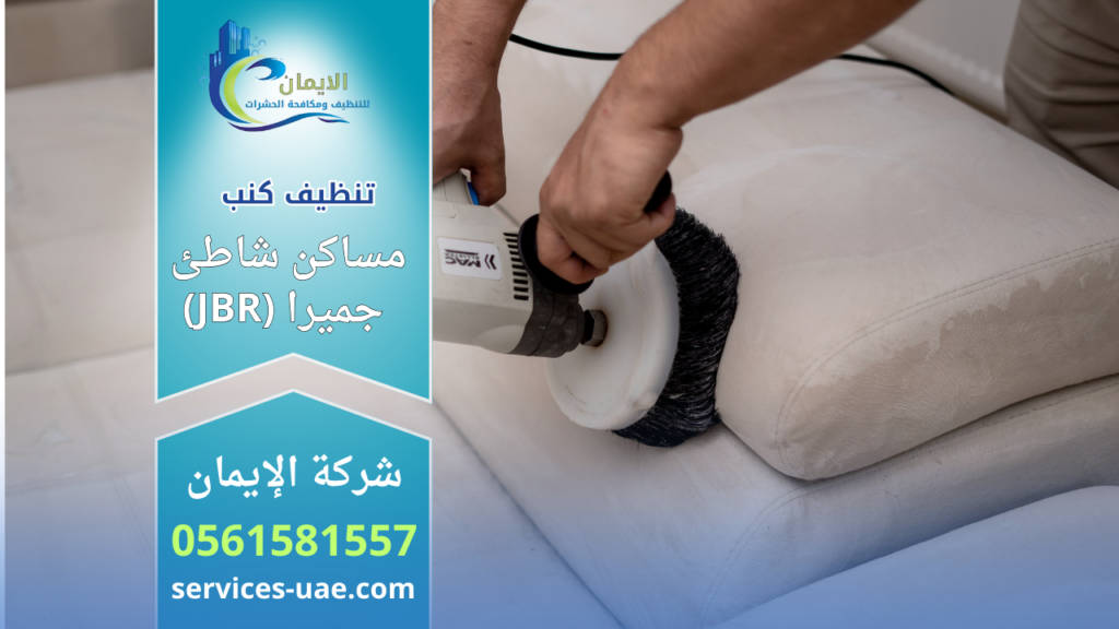 عامل يستخدم فرشاة كهربائية لتنظيف كنب قماشي ضمن خدمة شركة تنظيف كنب في مساكن شاطئ جميرا (JBR) داخل المنزل.